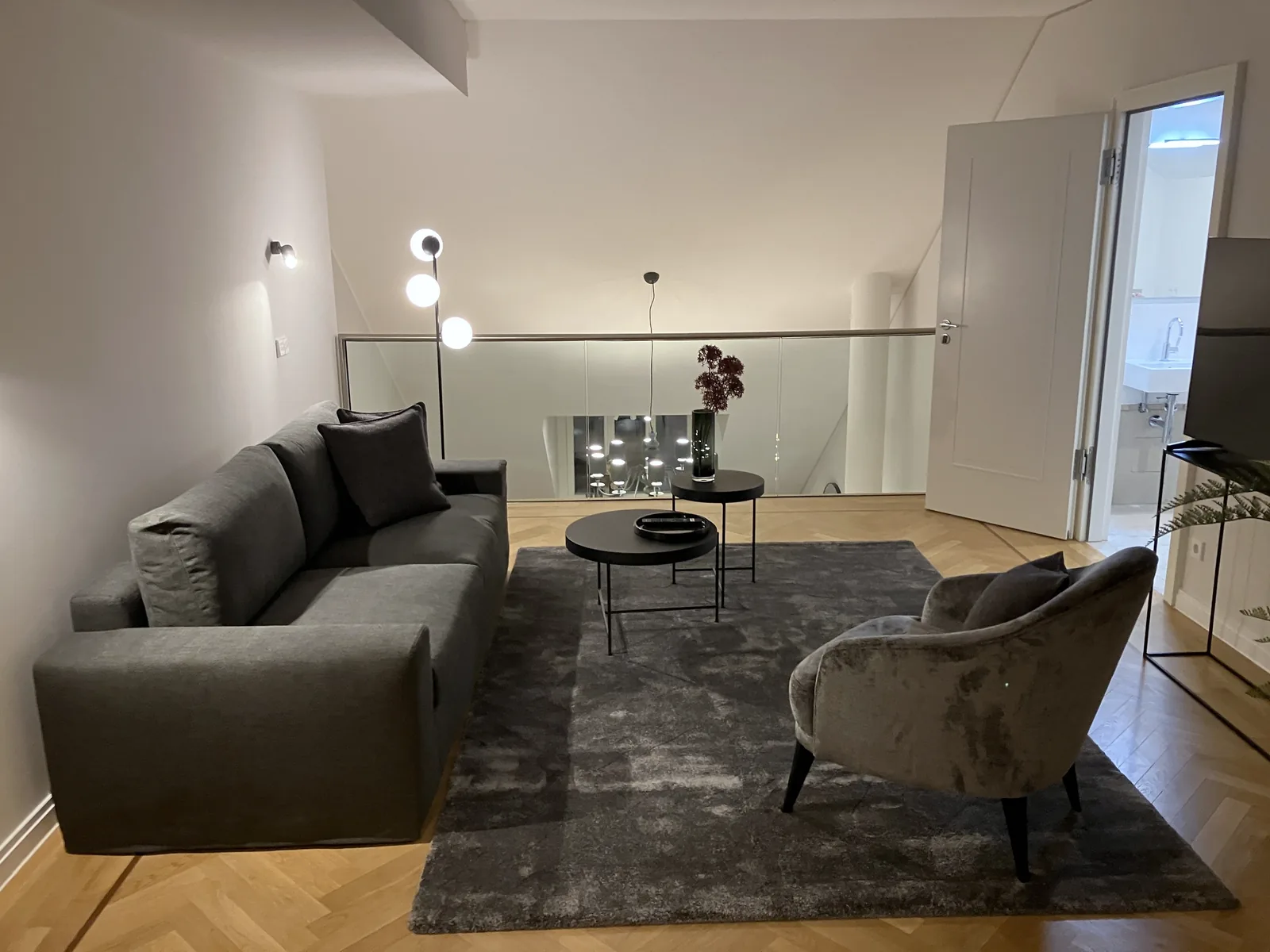 Galerie mit grauem Sofa, Samtsessel, Glasbrüstung und Blick in die untere Etage