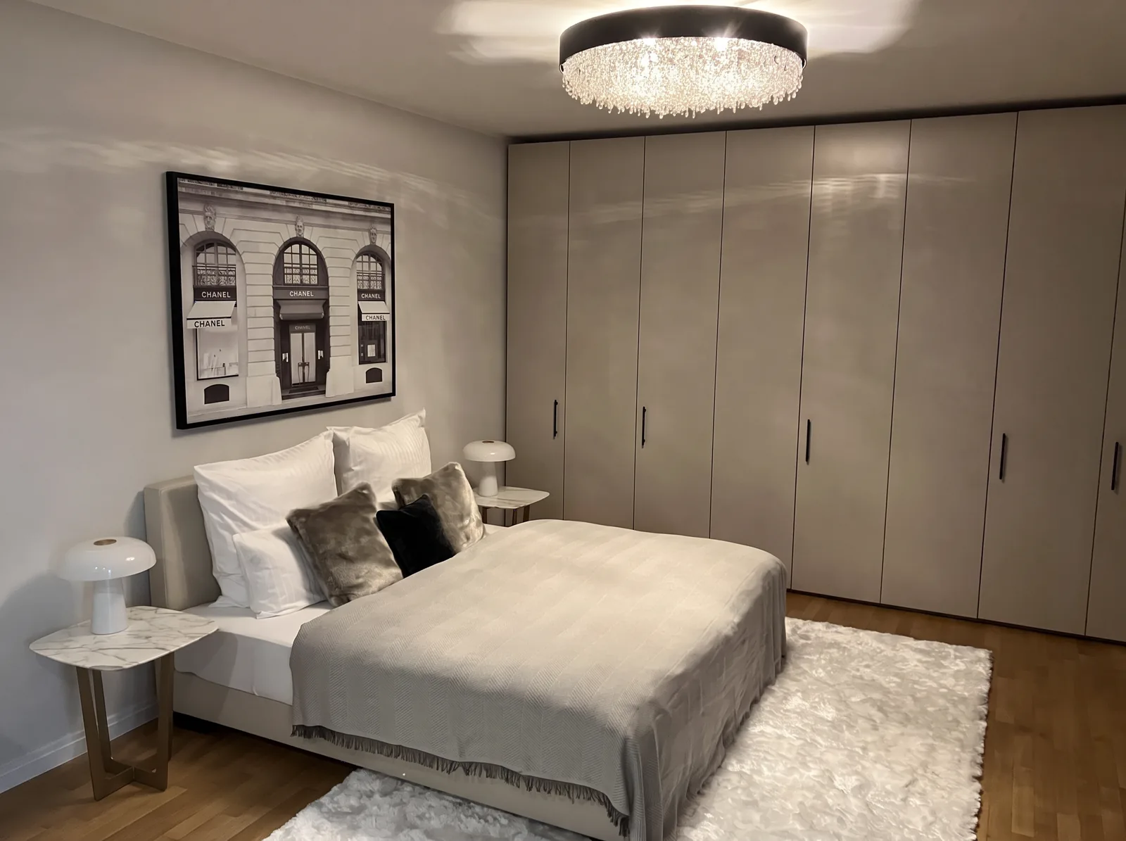 Schlafzimmer mit grauem Einbauschrank, Kristall-Deckenleuchte und Marmor-Nachttischen