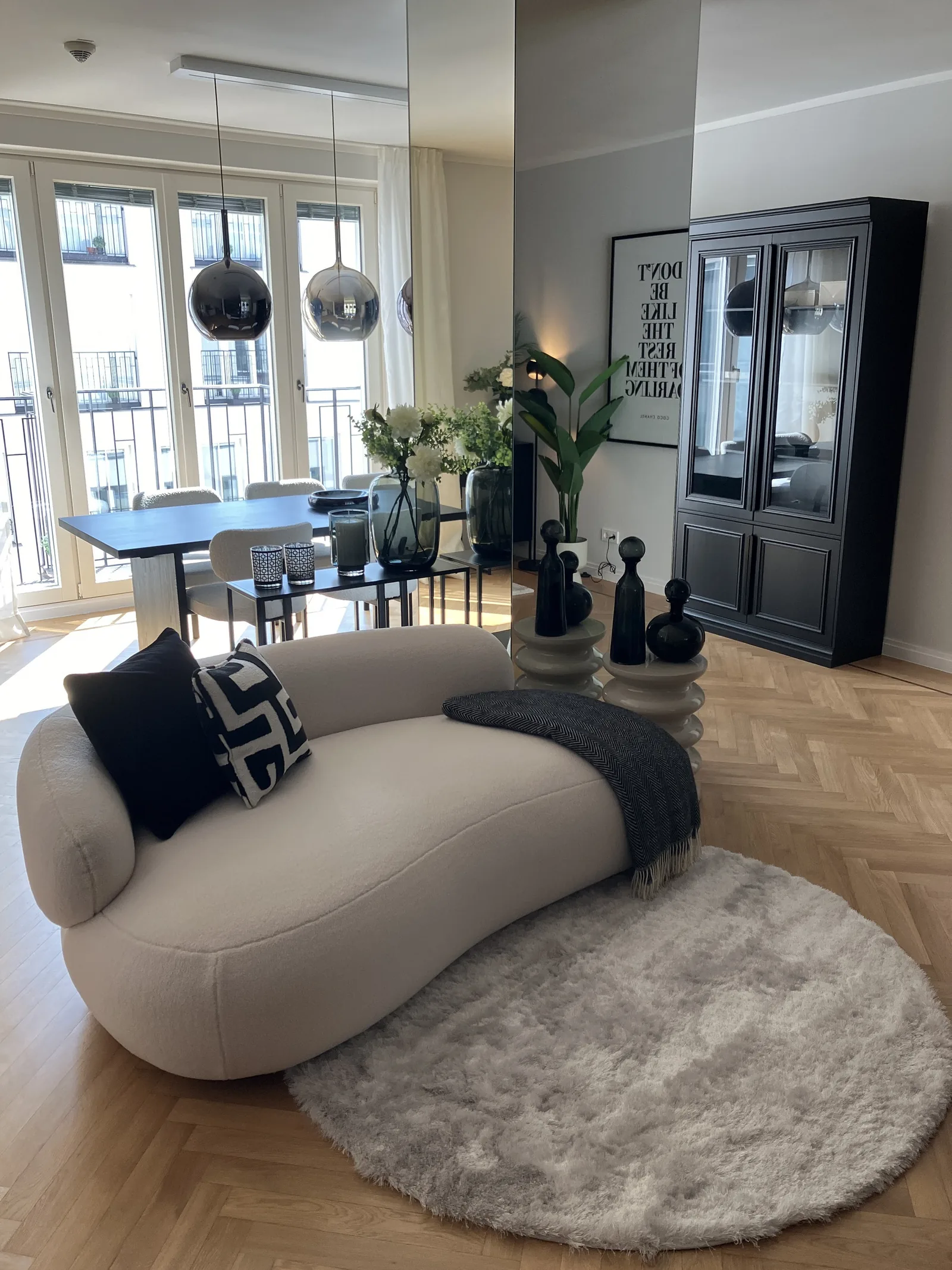 Geschwungenes Sofa in Bouclé vor Esstisch und schwarzer Vitrine, Blick auf den Balkon
