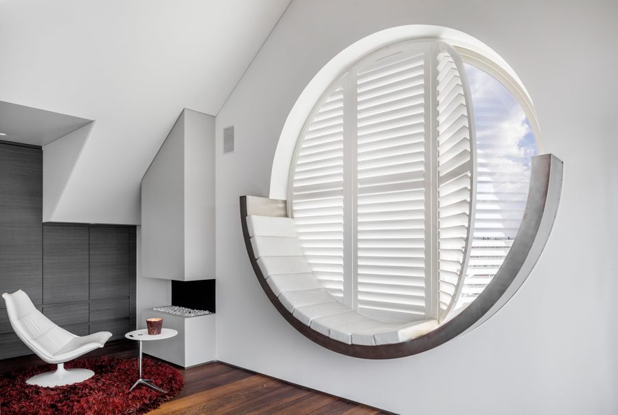 Rundes Fenster mit weißen Shutters in einem Dachzimmer