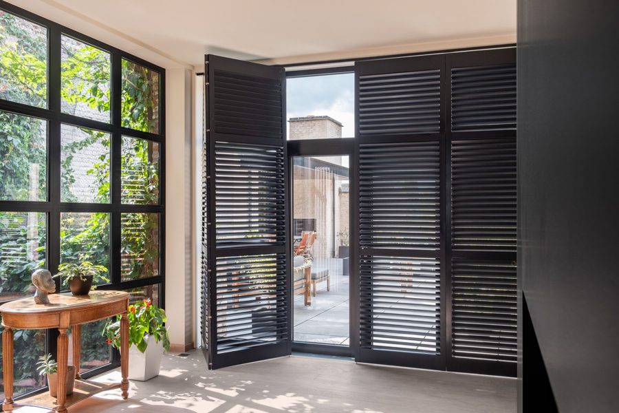 Schwarze Shutters an einer breiten Terrassentür, ein Flügel geöffnet